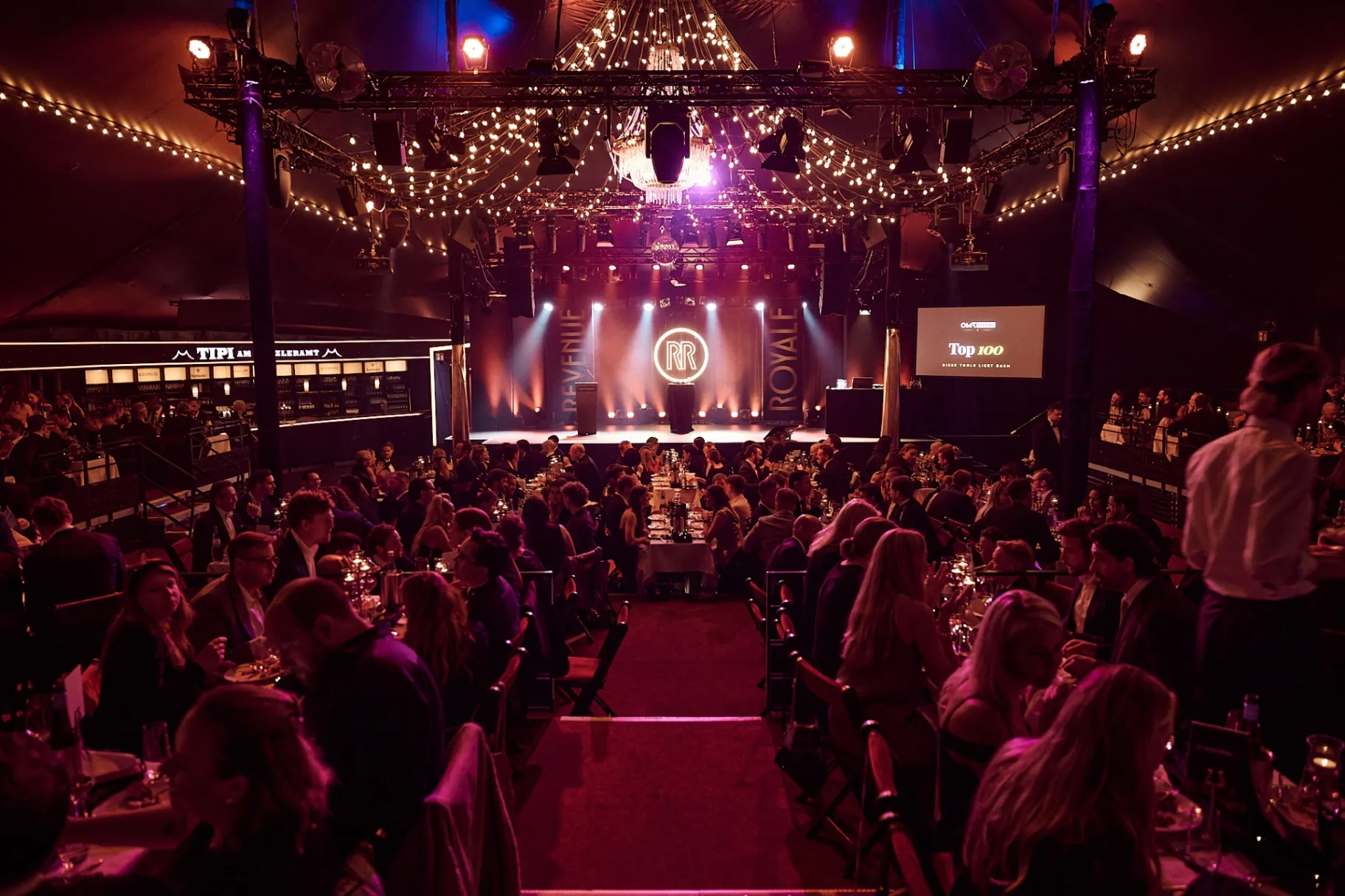 Revenue Royale 2026 Gala-Dinner – festlich beleuchteter Saal mit Bühnenlicht, Lichterketten und RR-Logo auf der Bühne